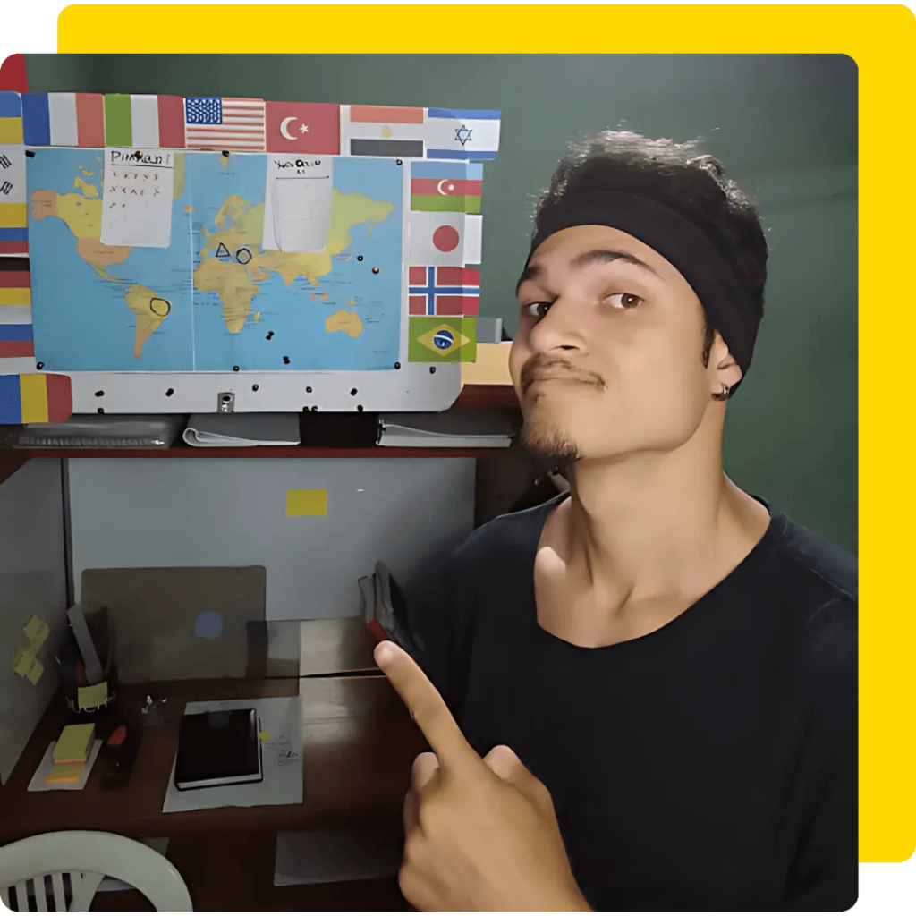 Gabriel Noah está no seu quarto de estudos, ele veste uma camiseta preta e uma bandana de mesma cor. Ele aponta para um mapa-múndi rodeado por bandeiras de vários países.