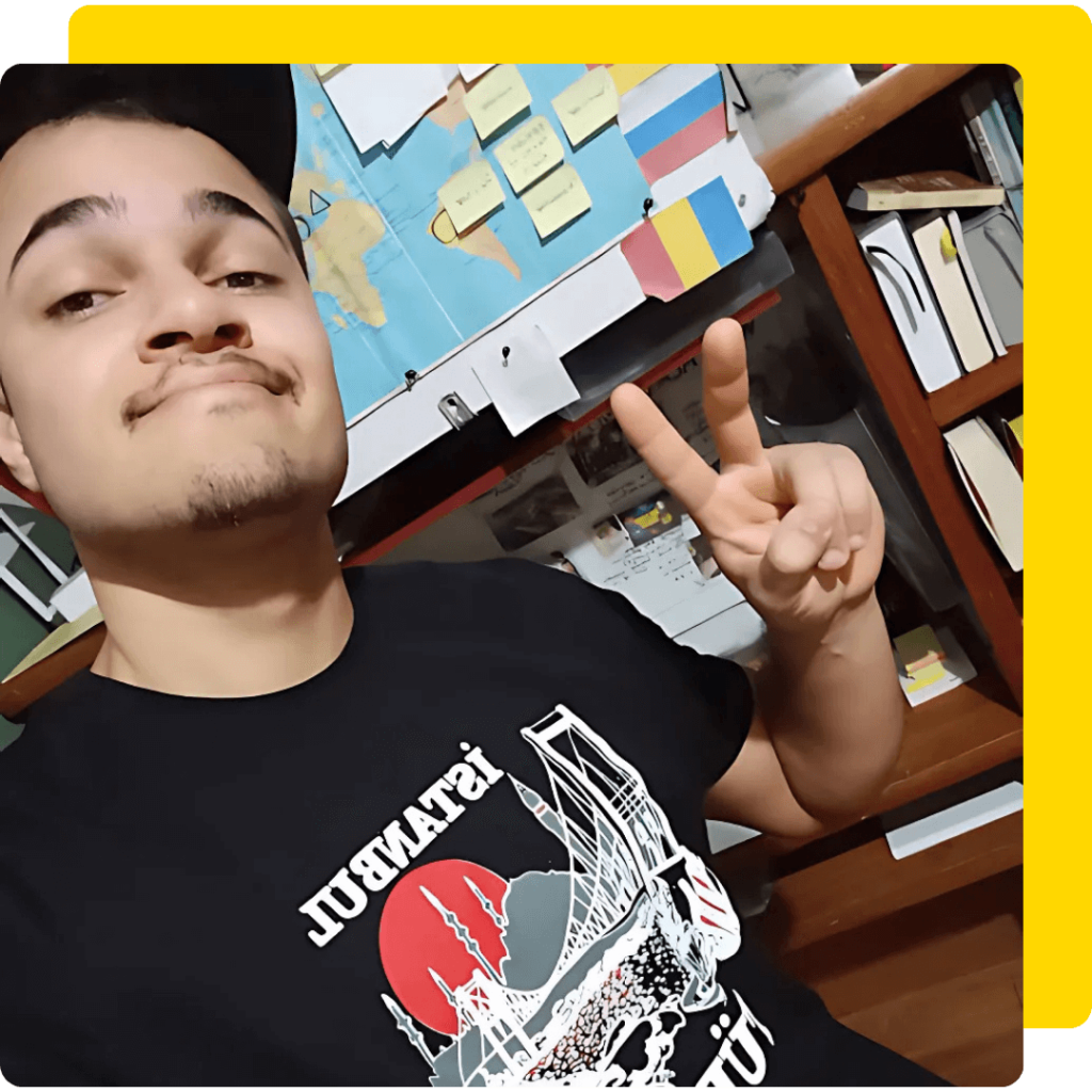 Gabriel Noah está em seu quarto de estudos, ele veste uma camiseta preta e usa um boné preto. Ele está próximo de sua escrivaninha cheia de livros e post-its.
